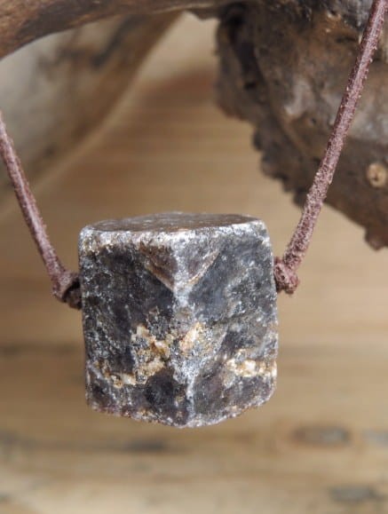 Korund na rzemieniu. Kryształ korundu - kamień naturalny - pojedynczy kryształ. Kamień nie jest szlifowany. Kamień przewiercony, zawieszony na skórzanym rzemyku w kolorze brązowym.