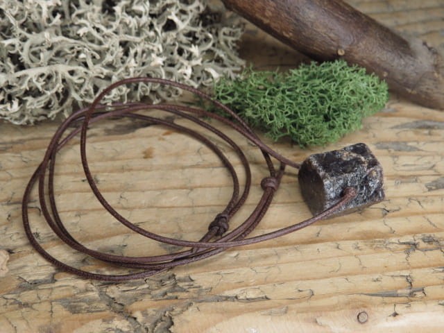 Korund na rzemieniu. Kryształ korundu - kamień naturalny - pojedynczy kryształ. Kamień nie jest szlifowany. Kamień przewiercony, zawieszony na skórzanym rzemyku w kolorze brązowym.