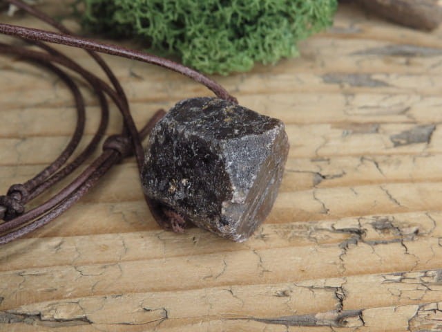 Korund na rzemieniu. Kryształ korundu - kamień naturalny - pojedynczy kryształ. Kamień nie jest szlifowany. Kamień przewiercony, zawieszony na skórzanym rzemyku w kolorze brązowym.