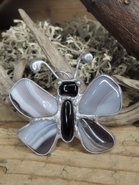 Wyjątkowy, ręcznie wykonany wisior artystyczny w kształcie motylka, stworzony z naturalnych kamieni: agatu i onyksu (środek). Całość została oprawiona w miedź i cynę, co nadaje kompozycji szlachetnego charakteru i surowego uroku.