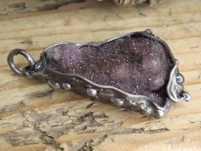 Wisiorek z surowego ametystu oprawionego w miedź i cynę. Ten wyjątkowy wisiorek łączy w sobie naturalne piękno ametystu i artystyczne rzemiosło.