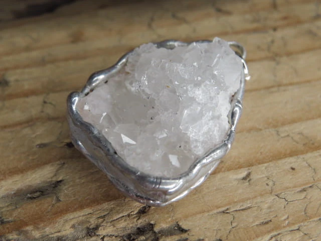 Ręcznie wykonany wisior z naturalną szczotką krystaliczną kryształu górskiego. Liczne, błyszczące kryształki tworzą efektowną, trójwymiarową strukturę, która pięknie odbija światło i podkreśla naturalne piękno minerału.