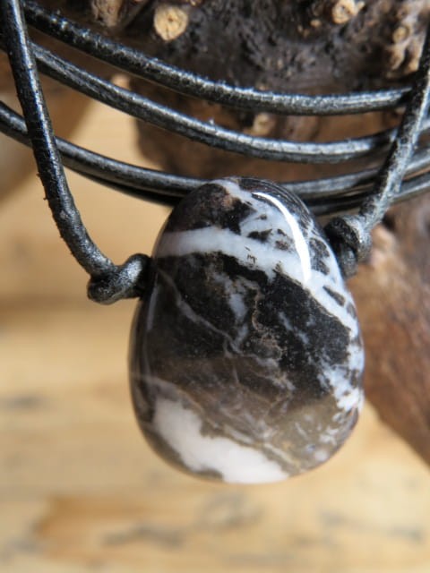 Amulet z marmuru zebra (jaspisu zebra). Kamień płaski, przewiercony, na czarnym rzemieniu o regulowanej długości. Talizman odwagi i motywacji.