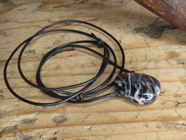 Amulet z marmuru zebra (jaspisu zebra). Kamień płaski, przewiercony, na czarnym rzemieniu o regulowanej długości. Talizman odwagi i motywacji.