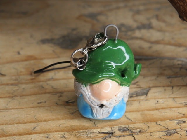 Ręcznie robiony skrzat z ceramiki – zawieszka na choinkę lub figurka stojąca. Zielona czapka, niebieskie ubranko, siwa broda. Świąteczny klimat. Kolorowy krasnal – ozdoba i prezent handmade.